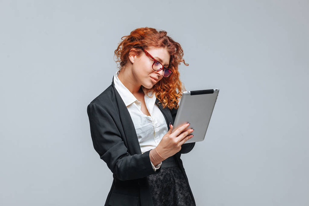Menina de cabelos vermelhos com um tablet em um fundo cinza claro
 - Foto, Imagem