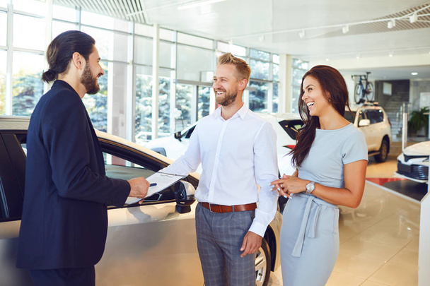 A car salesman and a buyer shake hands. A couple buys a car - Fotografie, Obrázek