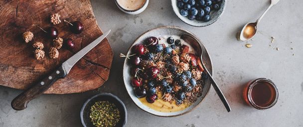 Healthy vegan breakfast. Flat-lay of quinoa oat granola coconut yogurt bowl with fruit, seed, nut, berries and cup of coffee over table background, top view, wide composition. Clean eating food concept - Fotó, kép