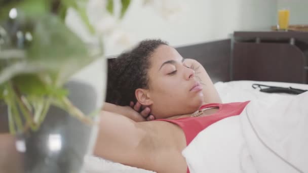 Cute African American woman lying in the bed, vase on table, video  - Filmagem, Vídeo