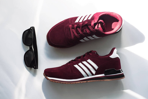 Burgundy sneakers on a white background with nature light shadows. - Photo, Image