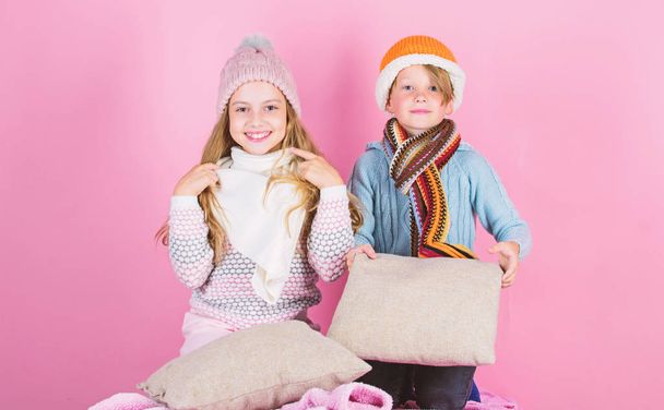 Children boy and girl warm up with pillows and hats. Stay warm and comfortable. Warm up your winter wear with cute and cozy accessories. Siblings wear winter warm hats sit on pink background - Foto, imagen