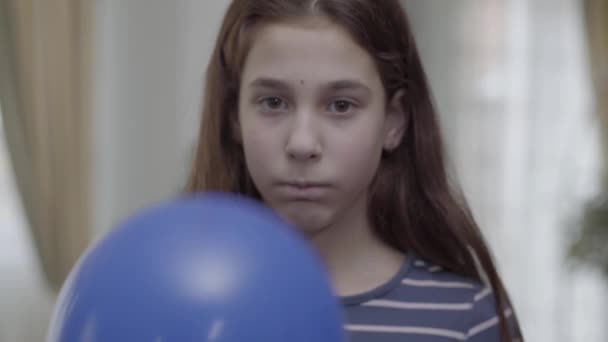 A pretty girl hiding behind blue balloon with a painted sad face on it then puts it down. The child is unhappy. Difficulties of being teenager - Séquence, vidéo