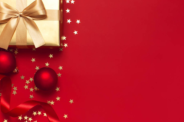 Nowy rok Christmas złote prezenty z wstążką, bombki, Złote gwiazdki konfetti na czerwonym tle widok z góry. Płaski lay Xmas święto 2020 uroczystości. Pudełka upominkowe karty okolicznościowe Dekoracje świąteczne - Zdjęcie, obraz