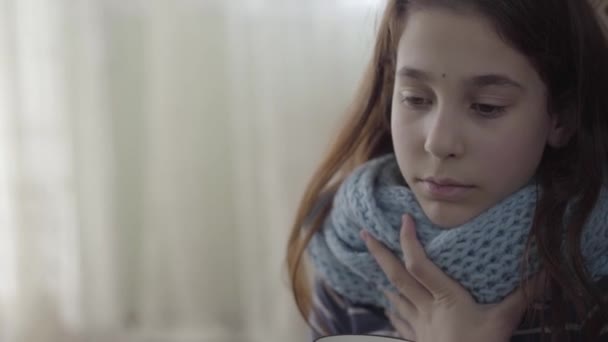 Portrait of a teenage girl wrapped in a warm scarf holding a cup of hot tea in hands. The girl feels bad, she is ill and has a fever. Concept of healthcare, treatment - Filmagem, Vídeo