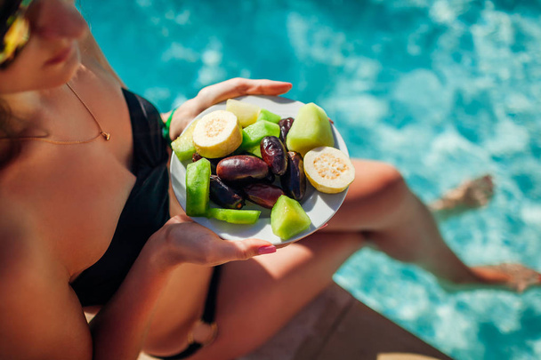 Donna in bikini che mangia frutta e si rilassa in piscina. All inclusive. Vacanze estive
 - Foto, immagini