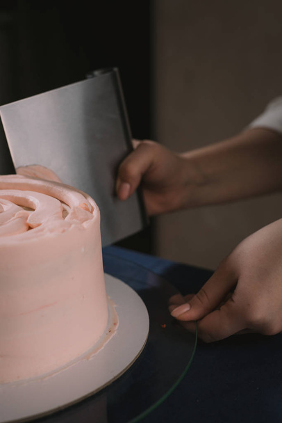Кондитер вирівнює крем шпателем. Майстер тортів лінії вершків на бежевому весільному торті
. - Фото, зображення