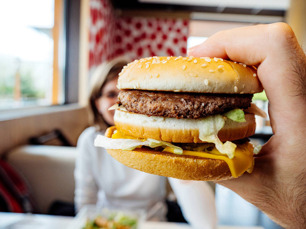 Mano masculina sosteniendo deliciosa hamburguesa doble mujer en segundo plano
 - Foto, imagen