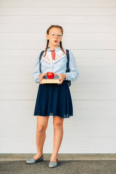 Happy little schoolgirl with book and red apple, wearing blue vintage blouse and  eyeglasses. Back to school concept - Photo, Image