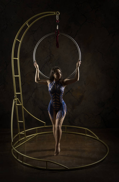 Prachtig meisje, luchtacrobatiek, podium in blauwe jurk neemt de acrobatische elementen op de draagbare lucht ring, in podium verlichting. - Foto, afbeelding