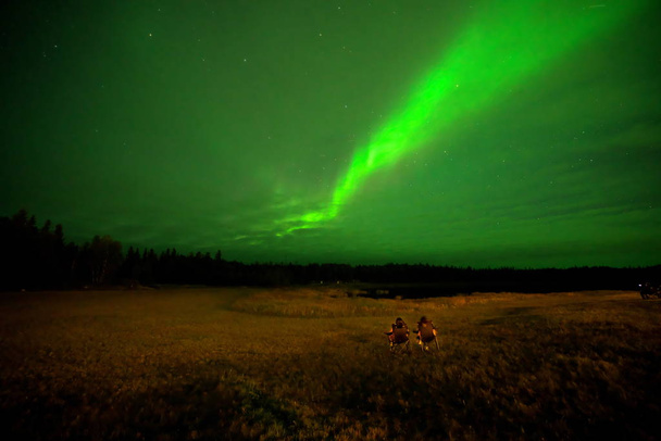 Yellowknife,Canada-August, 2019: Two men on a chair watching Aurora borealis or Northern lights in Yellowknife, Canada, on August, 2019 - Photo, Image