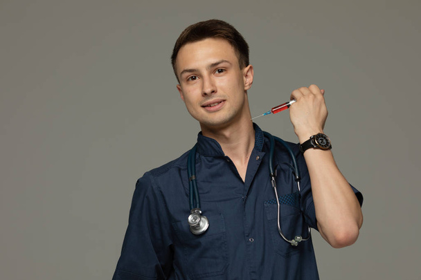Portrait of doctor holding syringe with injection and looking at camera isolated on grey background. - Foto, imagen