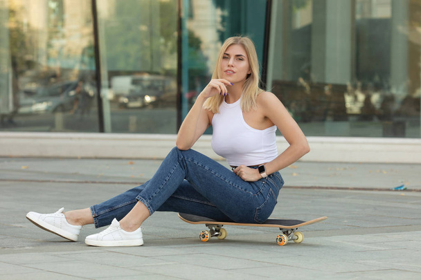 Closeup portrait of pretty blonde woman in casual outfit with skateboard posing in city - Φωτογραφία, εικόνα