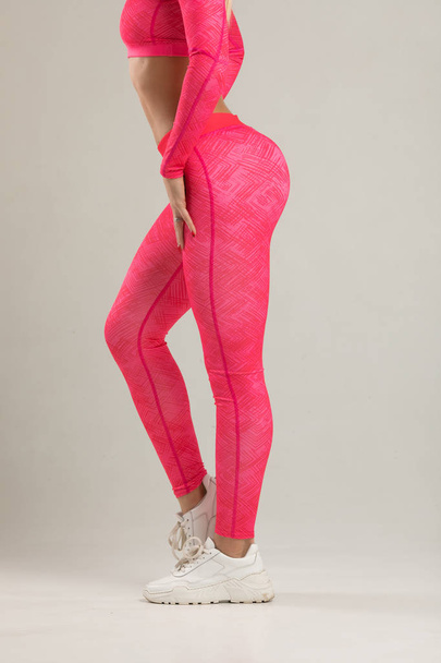 Young blonde fit woman in bright pink sportswear posing in studio - Foto, afbeelding