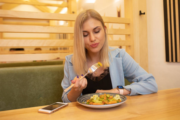 Gorgeous smiling young woman eating stewed vegetables at cafeteria.  - Zdjęcie, obraz