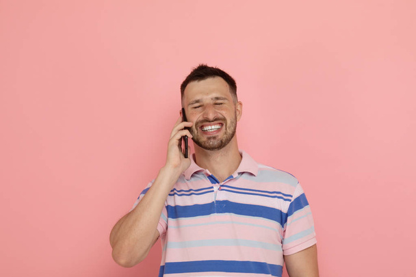 Молодой человек с помощью смартфона позирует на розовом фоне
 - Фото, изображение