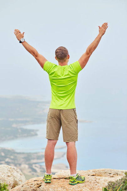 Молодой человек на вершине горы поднял руки вверх, держа метр
 - Фото, изображение
