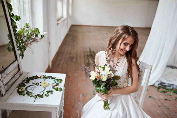 明るいスタイリッシュなスタジオでウェディングドレスで美しい花嫁。ヨーロッパスタイルの結婚式。手に装飾と花束. - 写真・画像