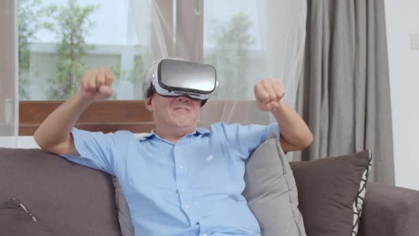 Os homens idosos asiáticos jogam jogos em casa. Asiático idoso chinês masculino feliz divertido e realidade virtual, VR jogar jogos enquanto deitado sofá na sala de estar em casa conceito. Tiro em câmara lenta
. - Filmagem, Vídeo