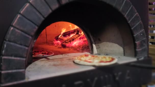 kuchař uvádí v pizzerii syrové pizzy do cihlové pece - Záběry, video