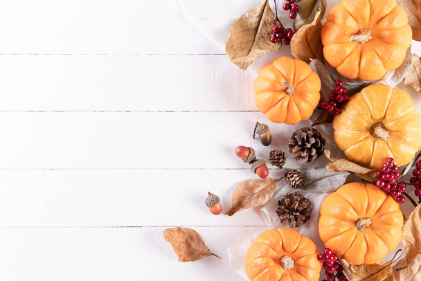 Vista superior de las hojas de arce de otoño con calabaza y bayas rojas sobre fondo de madera blanca. Concepto del día de Acción de Gracias
. - Foto, imagen