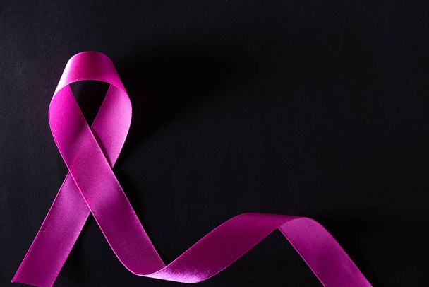 Pink ribbon on black paper background for supporting breast cancer awareness month campaign. - 写真・画像