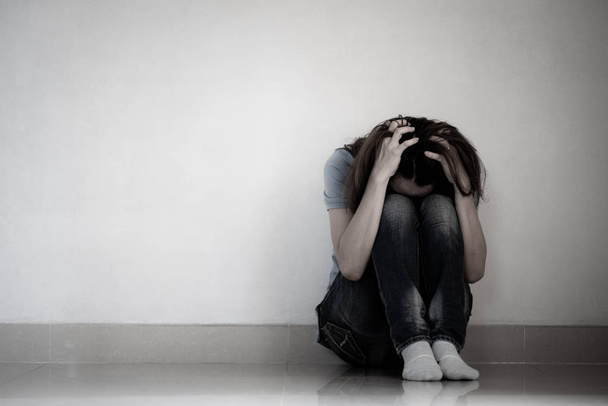 Traurige Frau umarmt ihr Knie und weint. Traurige Frau sitzt allein in einem leeren Raum. - Foto, Bild