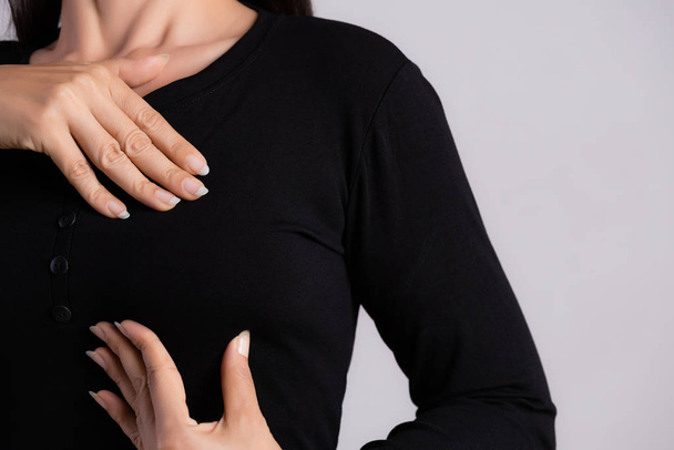 Mulher mão verificando pedaços em seu peito para sinais de câncer de mama em fundo cinza. Conceito de saúde. - Foto, Imagem