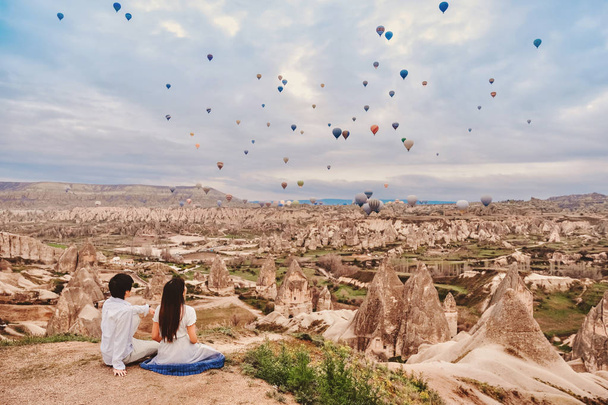 カラフルな熱気球が上空を飛んでいるのを見ているアジアのカップル  - 写真・画像