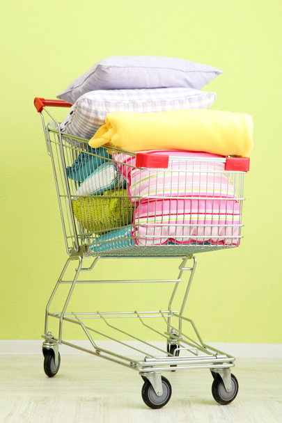 Carrito de compras con almohadas, sobre fondo de pared verde
 - Foto, Imagen