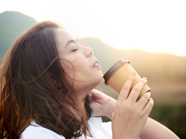 Emotional Asian woman drinking kng take away coffee cup with sun ligh
 - Фото, изображение