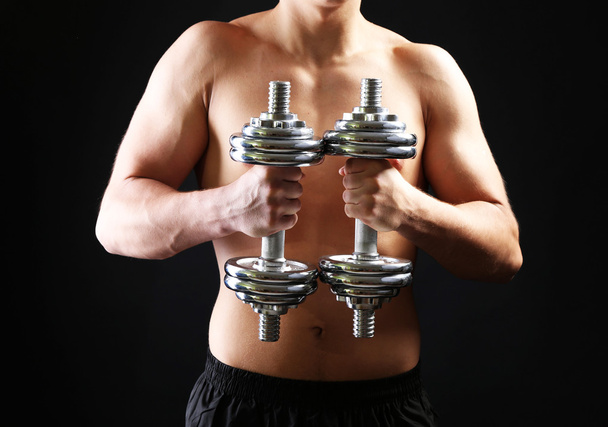 Handsome young muscular sportsman execute exercise with dumbbells on dark background - Fotografie, Obrázek