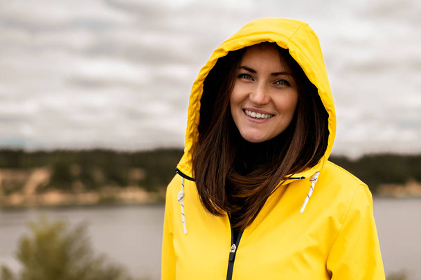 Πορτρέτο του χαμογελαστή κορίτσι με κίτρινη κουκούλα αδιάβροχο στο φόντο της λίμνης με χώρο αντιγραφής - Φωτογραφία, εικόνα