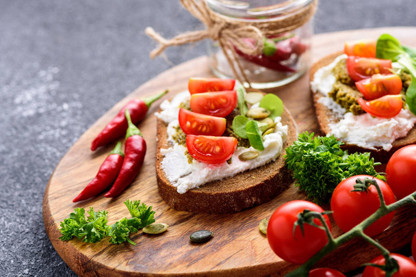 Kanapki z serem ricotta i pesto z pomidorkami wiśniowym, chilli i ziołami na drewnianej płycie - Zdjęcie, obraz