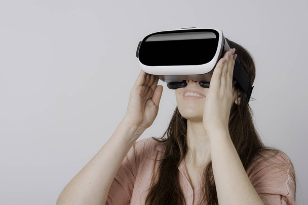 Жінка за допомогою VR пристрою тримає в обидві руки посміхаючись і дивлячись вгору
. - Фото, зображення