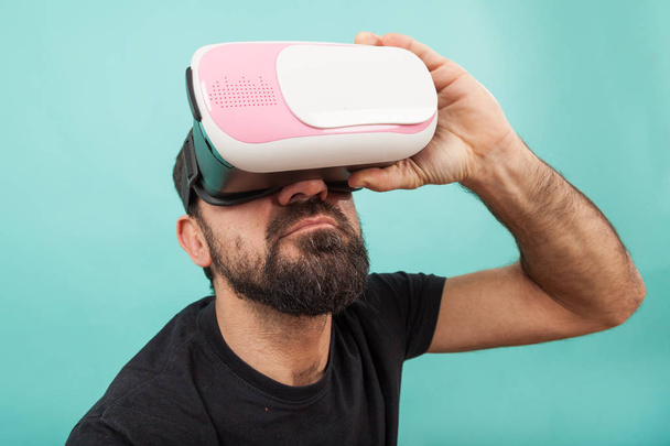 Ο μουσάτος χρησιμοποιεί γυαλιά εικονικής πραγματικότητας, γυαλιά. Ο τύπος στο ακουστικό VR κοιτάζει τη διαδραστική οθόνη. Αναπαραγωγή εφαρμογής κινητού παιχνιδιού στη συσκευή. - Φωτογραφία, εικόνα