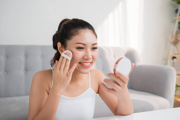 Retrato de una belleza joven cosmética mirando en el espejo usando esponja con polvo
. - Foto, imagen