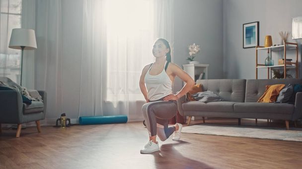 Strong and Beautiful Athletic Fitness Girl in Sportswear is Doing Forward Lunge Exercises in Her Bright and Spacious Living Room with Minimalistic Interior. - Foto, afbeelding