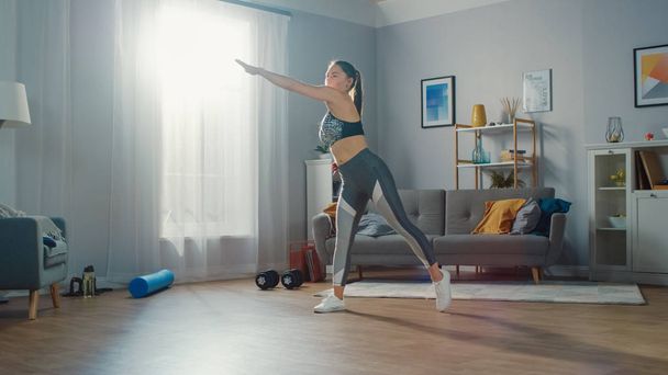 Shapely and Beautiful Athletic Fitness Girl in Sportswear is Doing Cardio Exercises in Her Bright and Spacious Living Room with Minimalistic Interior. - Фото, изображение