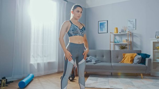 Shot of a Fit Beautiful Female in an Athletic Top Doing Breathing Exercises in Her Bright and Spacious Living Room with Minimalistic Interior. - Foto, imagen