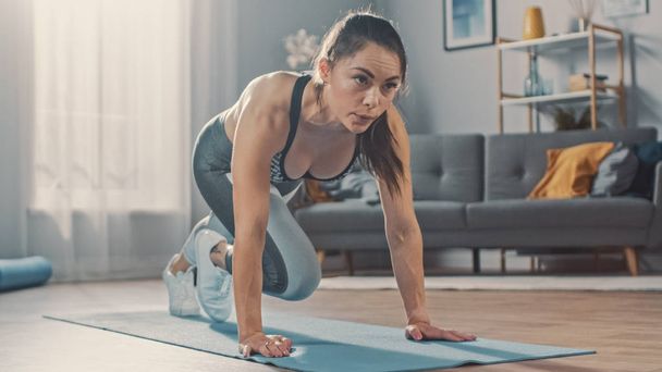 Shot of a Beautiful Confident Strong Fitness Female in a Grey Athletic Outfit is Doing Mountain Climber Exercises in Her Bright and Spacious Apartment with Cozy Minimalistic Interior. - Valokuva, kuva