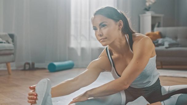 Beautiful Confident Fitness Girl in an Athletic Workout Clothes is Doing Stretching Yoga Exercises in Her Bright and Spacious Living Room with Cozy Minimalistic Interior. - Zdjęcie, obraz
