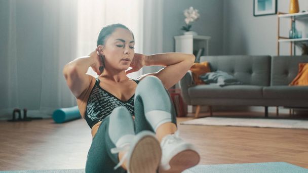 Strong and Fit Beautiful Busty Girl in an Athletic Top is Doing Crisscross Crunch Workout in Her Bright and Spacious Living Room with Minimalistic Interior. - 写真・画像