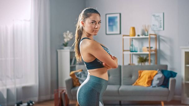 Strong and Fit Beautiful Busty Girl in an Athletic Top is Posing With a Soft Smile Showing Her Figure. Bright and Spacious Living Room with Minimalistic Interior. - Foto, afbeelding