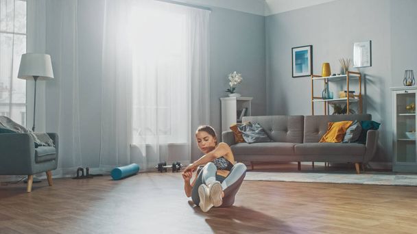 Strong and Fit Beautiful Girl in a Grey Athletic Outfit Energetically Exercising in Her Bright and Spacious Living Room with Minimalistic Interior. - Foto, Imagen