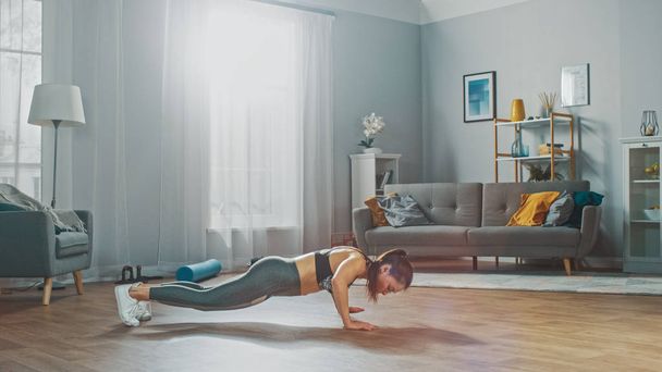Strong and Fit Beautiful Girl in a Grey Athletic Outfit Energetically Exercising in Her Bright and Spacious Living Room with Minimalistic Interior. - Foto, Imagem