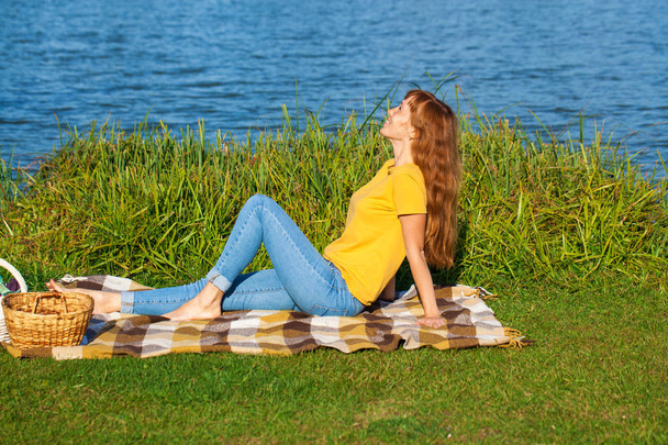 Young red-haired woman resting on the lawn near the lake - Foto, immagini