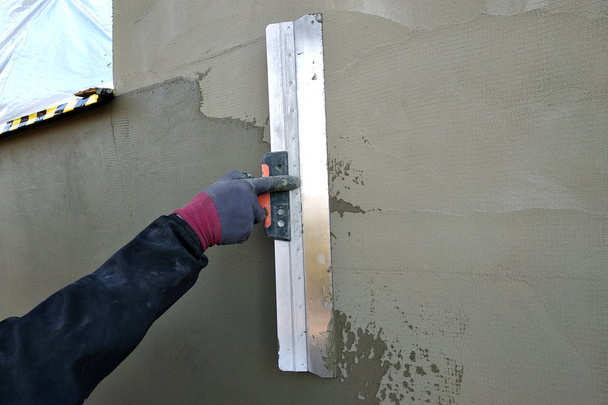 Trabalhador que cobre parede isolada com solução de cola sobre plaste
 - Foto, Imagem