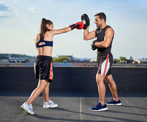 Young boxer girl with her coach hitting mitts outdoor on a roof in urban environment - Foto, Imagem