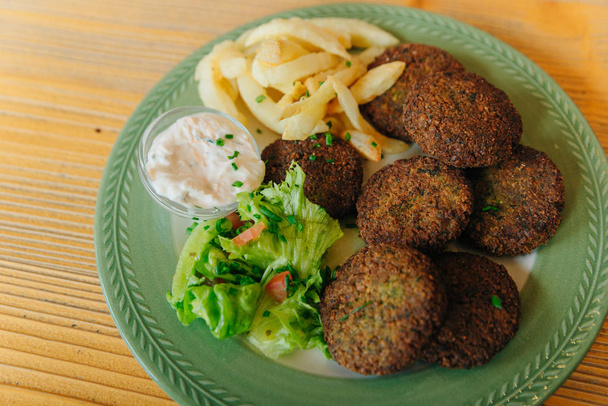 Spicy bifteki, frikadelle or frikkadel meatballs with minced beef and lamb with pita bread, tzatziki dip, vegetables salad and French fries. Greek meatballs keftedes or Keftedakia. - Photo, Image